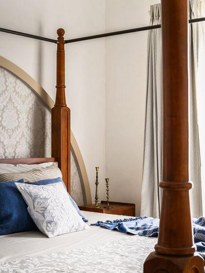 A close-up of the four-poster bed, showing the turned wood detail of the post and the subtle pattern on the headboard. These details add a layer of craftsmanship and elegance to the room.