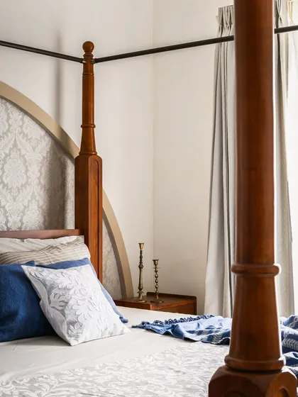 A close-up of the four-poster bed, showing the turned wood detail of the posts and the subtle damask pattern of the upholstered headboard.
