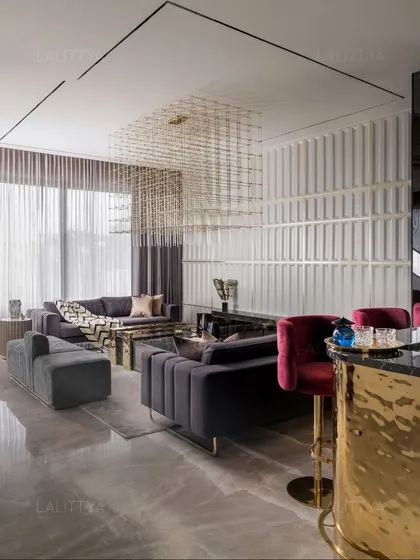 A look at the integrated bar and lounge area, where a statement brass-clad bar with red velvet stools provides a vibrant focal point. The seating area features channel-tufted grey sofas under a sculptural chandelier, with a fluted wall panel adding texture and rhythm.