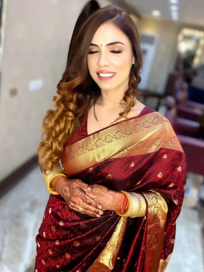 A happy client glowing in a traditional silk saree, with her hair styled in soft, cascading curls.
