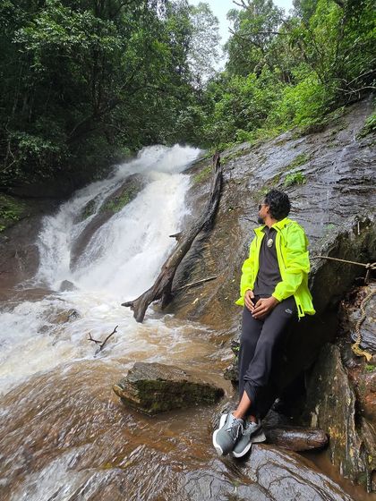 A trekker sits peacefully by a stream on the Kodachadri trail, surrounded by lush greenery.