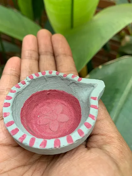 Another view of the pink and grey diya, showing the texture of the clay and the hand-painted details along the rim.