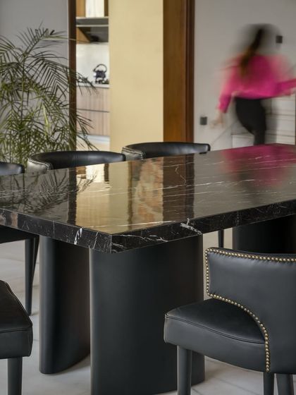 A detail of the dining area, showing the contrast between the heavy black marble table and the soft, organic forms of the chairs. The space is a study in contrasts, balancing bold statements with quiet elegance.