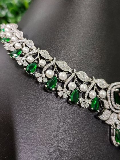 A close-up of the intricate design, combining sparkling AD stones, rich green gems, and classic pearls.