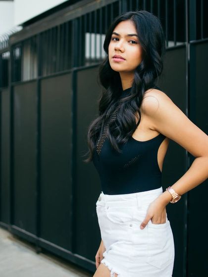 A simple and clean urban portrait against a dark metal fence. The contrast between the subject's white shorts and the black background makes this a striking and modern lifestyle shot.