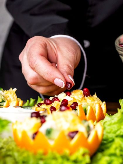 The art of plating. A chef carefully garnishes a salad served in a hollowed-out orange with pomegranate seeds, showing the creative detail we put into our food presentation.