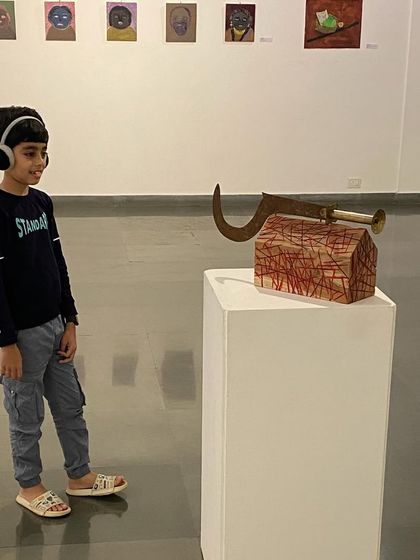 A young visitor wearing headphones interacts with a sound-based sculpture by Unnikrishnan C. from the 'ME, AMMA, WE' show, demonstrating the multi-sensory aspects of the exhibition.