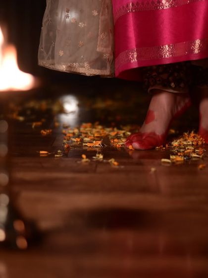 A close-up of feet adorned with 'alta' on a floor scattered with flower petals, with a traditional lamp nearby. This artistic shot evokes a sense of sacredness and ritual in dance.
