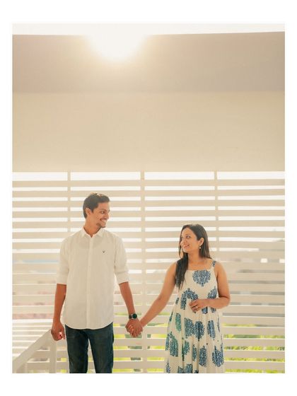 A simple, happy moment between Annalisa and John, holding hands against a backdrop of white louvers with the sun flaring above. The feeling is light, airy, and joyful.