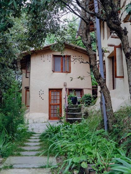 A view of one of the mud-and-stone cottages at the retreat, nestled amidst lush greenery. This is the quiet, sustainable haven I've built for writers.