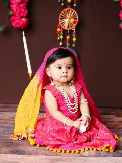 A serene portrait of the baby girl in her beautiful ethnic dress, surrounded by elegant candles and floral decor.