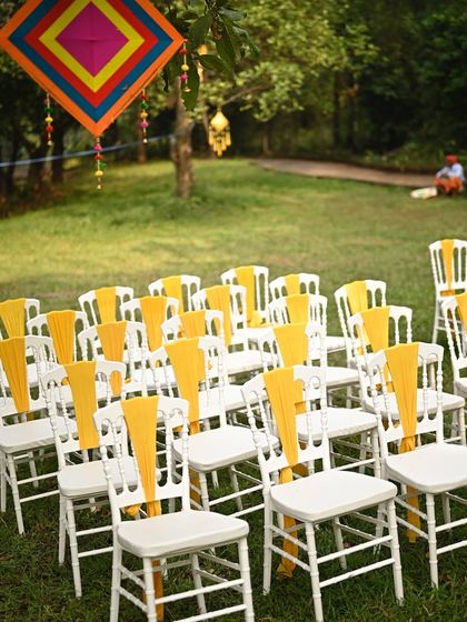 Guest seating for an outdoor Haldi, with white chairs adorned with bright yellow sashes to match the overall color theme.