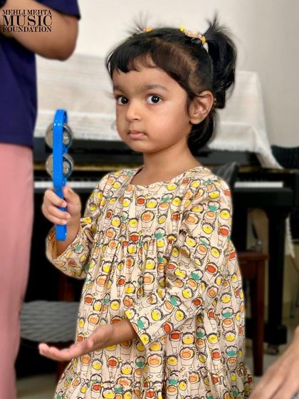 A toddler holds a shaker, learning about cause and effect through sound. Our classes are designed to stimulate cognitive development through musical play.