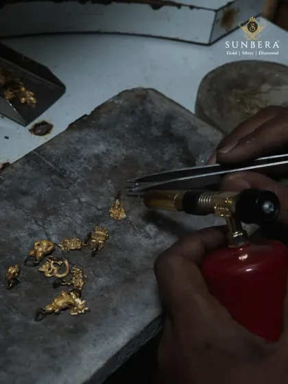 An artisan uses a torch to carefully solder small gold components. This traditional technique requires years of practice and is essential for creating strong, seamless, and intricate jewellery designs.