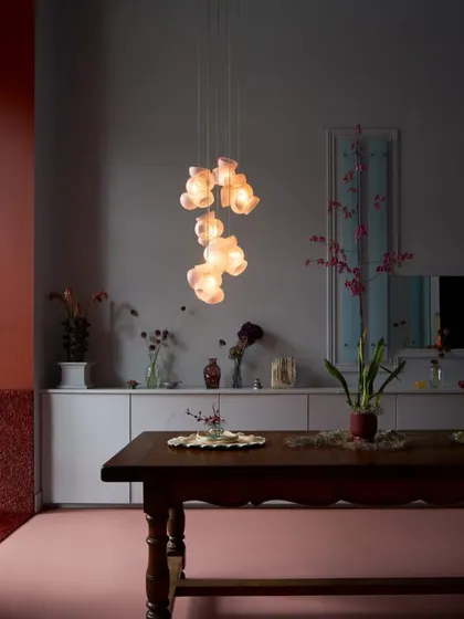 A vertical cluster of pink Bocci 100 pendants illuminates a dining space. The soft, warm light creates an inviting atmosphere, while the fixture itself serves as a piece of hanging art.