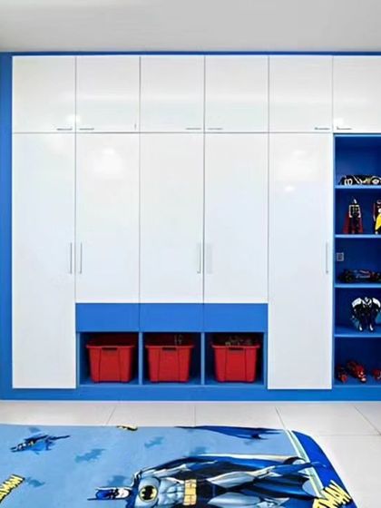 A large, built-in wardrobe for a child's room in a blue and white theme. It includes open shelving for toys and display items, along with lower cubbies for easy-to-reach storage bins.