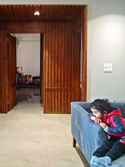 A view into a Gurgaon residence where stained pine wood panels create a warm, rhythmic entryway. The design divides a larger volume into smaller, functional 'pockets' without using solid walls.