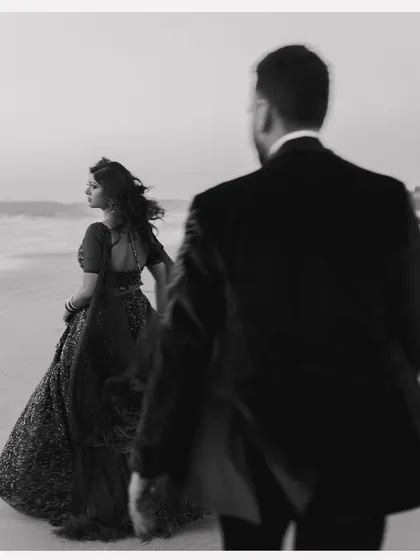 A black and white version of a beach portrait, this image feels moody and cinematic. The focus on the groom in the foreground with the bride in the distance creates a sense of story and intrigue.