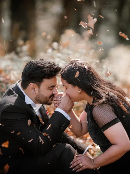 An intimate moment as a man kisses his partner's hand amidst a shower of falling autumn leaves, creating a romantic and timeless photograph.