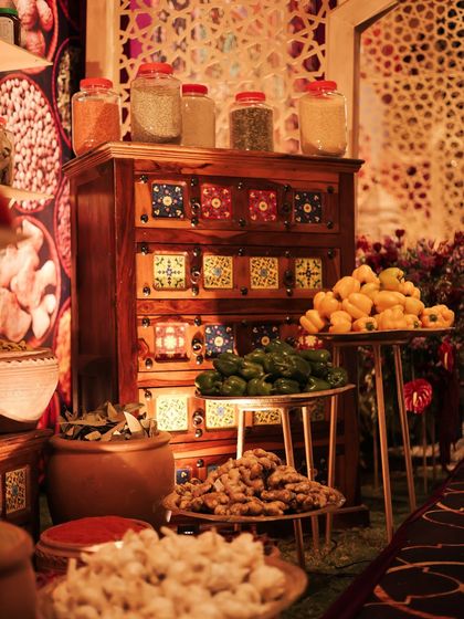A display of fresh vegetables and spices, including ginger, lemons, and green chilies, arranged on tiered stands. This brought a sense of a real, living marketplace to the sangeet decor.