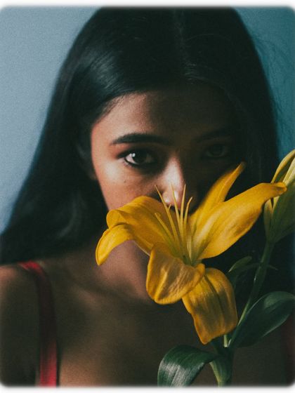 In this shot, the yellow flower is the main focus in the foreground, with the model's eyes peeking out from behind it. This creates a beautiful sense of depth and mystery, drawing the viewer into the image.
