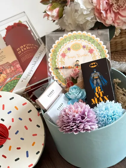 A cute and compact Rakhi hamper in an H&M storage box, including a Zara perfume, Carra chocolates, and a "super brother" rakhi.