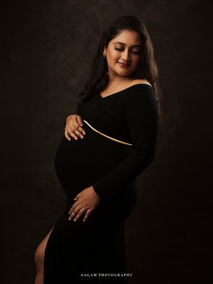 A moment of quiet reflection. The simple black dress and soft lighting create a sophisticated and timeless maternity portrait.