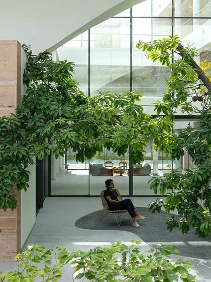 A quiet moment in a courtyard where a woman sits under a tree. The design uses the existing tree as a natural anchor, with minimalist paving and seating creating a space for pause and reflection.