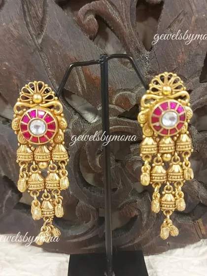 These Dakshinaya earrings feature a cascade of tiny gold jhumkis, or bells, creating a beautiful sound and movement. The central ruby-colored stone adds a touch of regal color.