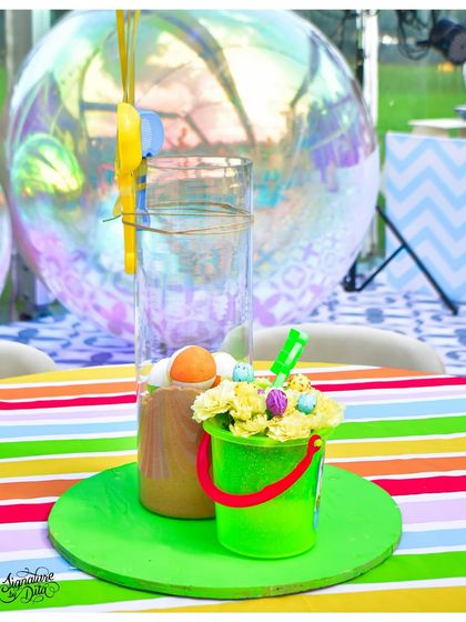 The little details matter. This table centrepiece for a summer carnival party includes a mini sand bucket with flowers and a colourful striped tablecloth, perfectly capturing the fun-in-the-sun theme.