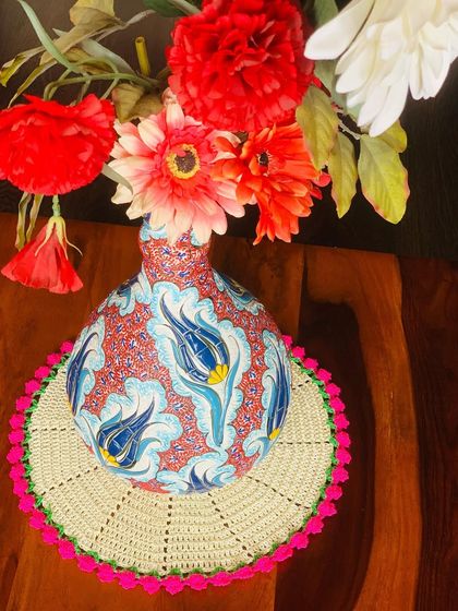 A cream doily with a bright pink tulip border, used here as a beautiful base for a colorful flower vase.