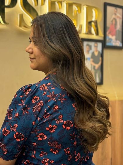 A side view of a client's balayage, showing how the color adds dimension and movement to her hair. The soft waves enhance the beautiful, blended tones.