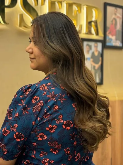 A beautiful balayage on long hair, with a seamless transition from dark roots to lighter ends, styled in soft, elegant waves.