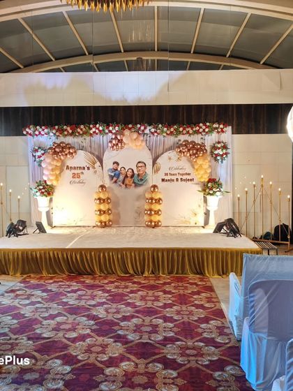 A grand stage for a 25th birthday and anniversary celebration. The backdrop features personalized panels with photos, surrounded by balloons and elegant lighting.