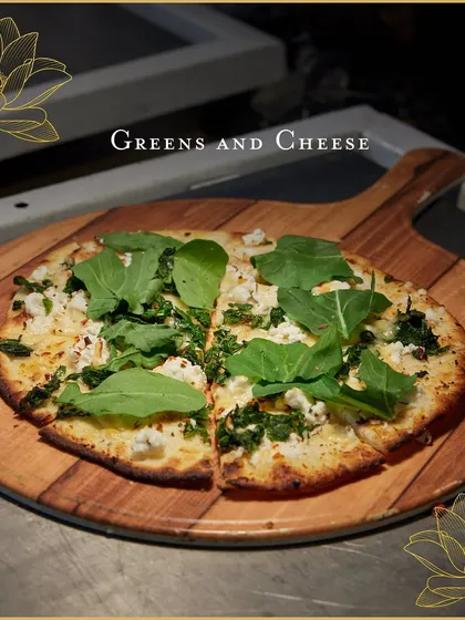 A freshly baked pizza with arugula and cheese, ready to be served from our live station. The wooden peel and simple presentation emphasize the artisanal quality of our food.