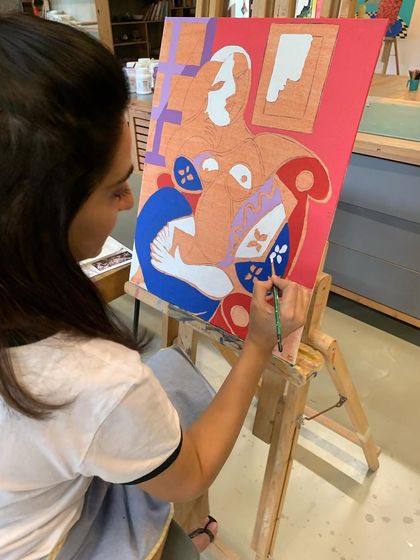 A student carefully paints her "Woman with Book," following the bold outlines and vibrant color blocking of Picasso's original.