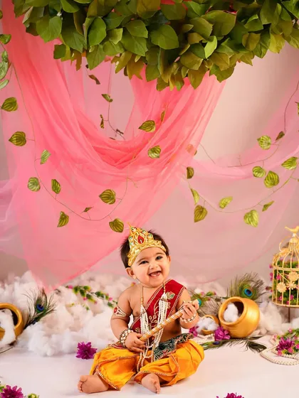 A wide shot of our beautiful Janmashtami setup, featuring a canopy of leaves and pink fabric. This little Krishna's happy smile makes the entire scene magical.