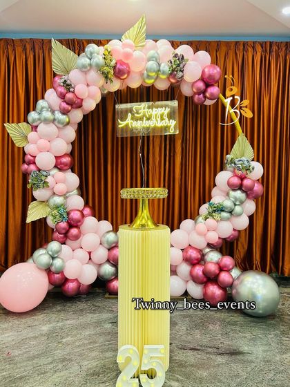 An elegant anniversary decoration with a circular balloon arch in shades of pink and silver. The "Happy Anniversary" neon sign and marquee number "25" complete this beautiful setup.