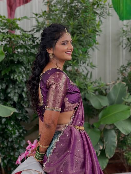 A side view of the bride's welcome look, showing her half-saree and curly ponytail hairstyle.