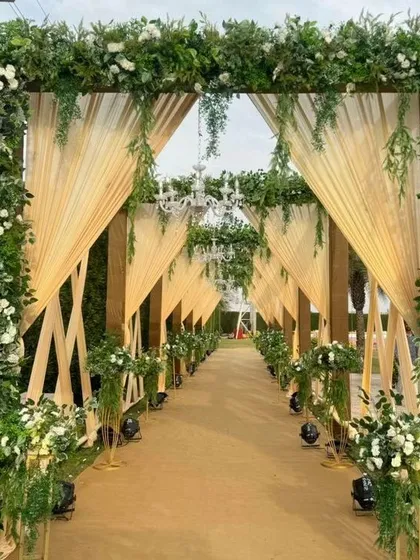 I design elegant walkways that make your guests feel special from the moment they arrive. This beautiful entrance features a long pathway lined with lush green and white floral arches and classic chandeliers for a sophisticated wedding reception.