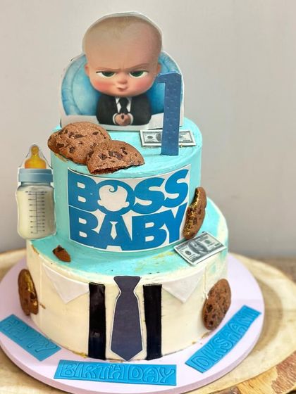 Another view of the Boss Baby cake, showing the fun details like the baby bottle, chocolate chip cookies, and edible dollar bills scattered around.