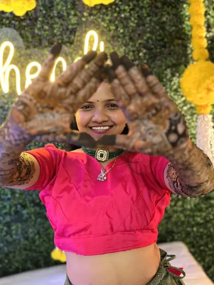 A happy bride posing for the camera. The combination of the green wall and yellow marigold tassels adds a fresh and festive touch.