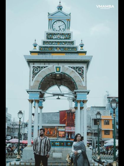 A vertical shot of a couple posing in front of a grand clock tower, emphasizing the height and architectural details of the location.
