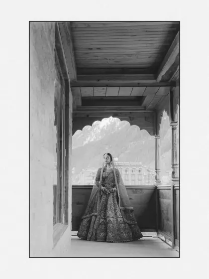 A stunning black and white bridal portrait. The bride is framed within a balcony, creating a sense of depth and drawing attention to her elegant silhouette against the mountain view.