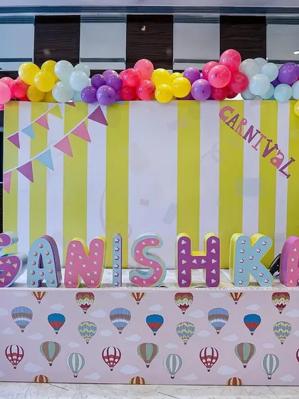 A cheerful carnival name display for "Ganishka." The setup includes a striped backdrop, colorful letters, and a hot-air-balloon-themed table skirt, creating a perfect photo corner.