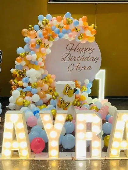 A butterfly-themed first birthday party with large marquee letters spelling 'AYRA' and colorful balloon columns.