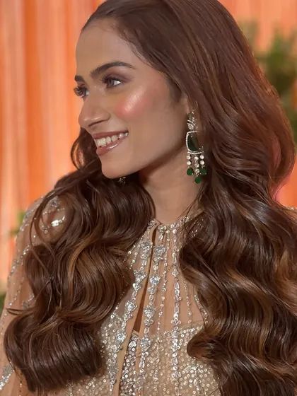 A smiling bride-to-be, with her hair styled in big, bouncy waves that perfectly complement her sparkling reception outfit.