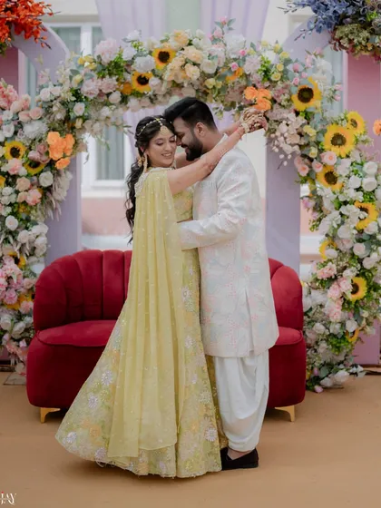 A sweet embrace between the couple in front of a beautiful pastel floral arch at their Haldi function.