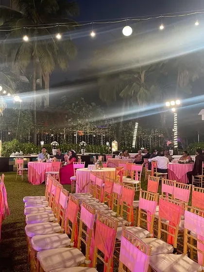 A beautiful pink-themed seating arrangement for an outdoor reception. The lawn is filled with elegantly decorated tables under a canopy of glowing lanterns.