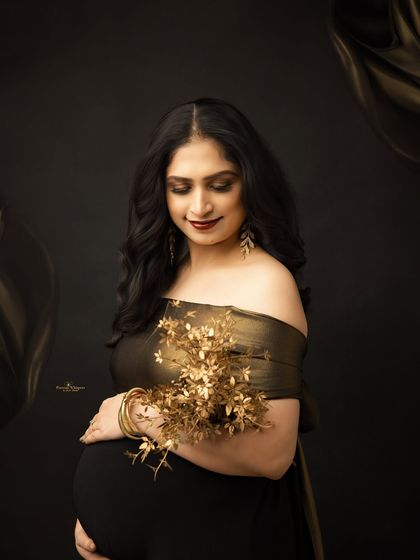 A serene solo portrait of a mother-to-be holding a golden bouquet. The dark, moody lighting and her gentle expression create a feeling of intimate and quiet joy.